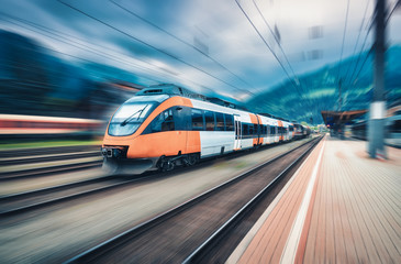 Obraz na płótnie Canvas High speed orange train in motion on the railway station at sunset. Modern intercity passenger train with motion blur effect on the railway platform. Industrial. Railroad in Europe. Transport