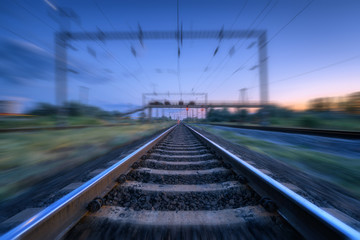 Fototapeta na wymiar Railroad and blue sunset sky with clouds with motion blur effect. Industrial landscape with railway station and blurred background at twilight. Railway platform in move. Transportation. Speed motion