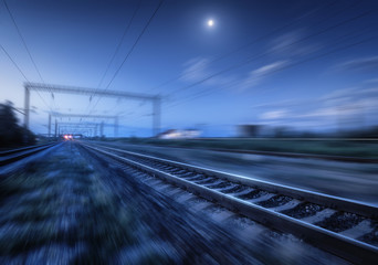 Railroad and blue sky with moon and clouds at night with motion blur effect. Industrial landscape with railway station and blurred background at twilight. Railway platform in move. Transportation