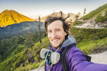 Young man tourist makes a selfie with the magnificent views on green mountains from a mountain road trecking to the Ijen volcano or Kawah Ijen on the Indonesian language. Famous volcano containing the