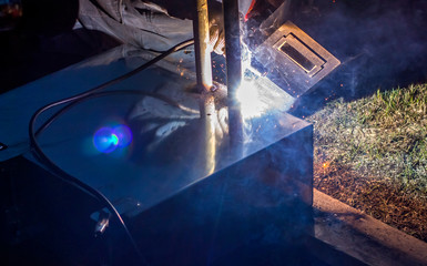 professional welder welds metal parts by electric welding, forming a bright light