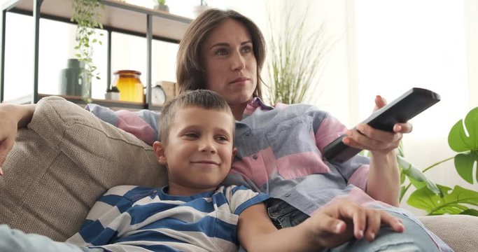 Relaxed mother and son laughing while watching tv at home