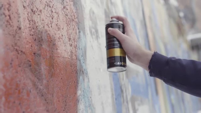 Hand holding a spray paint can and drawing colorful graffiti on the wall, street art concept. Action. Side view of an artist painting with aerosol spray on the wall, concrete paint work.