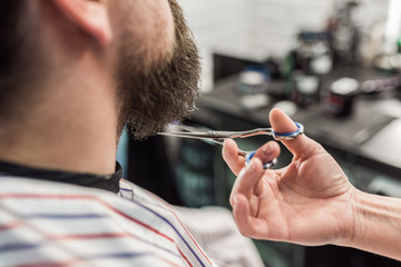 Hand of a barber cutting customer's beard with scissors.