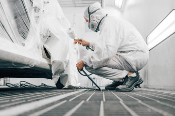 Painter in protective work wear painting car body, low angle image