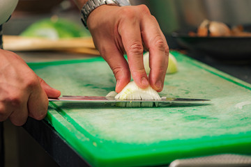 Hands of a male chef cutting onion.