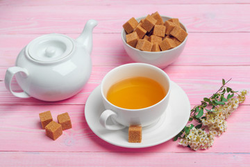 Cup of tea with sugar cubes and flower branches on wooden table close up