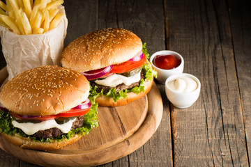 Close-up photo of home made hamburger with beer made of beef, onion, tomato, lettuce, cheese and spices. Fresh burger closeup on wooden rustic table with potato fries and chips.