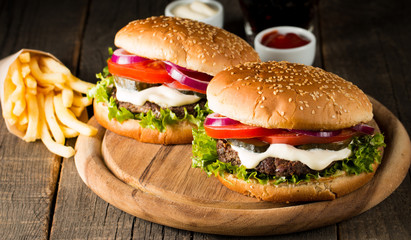 Close-up photo of home made hamburger with beer made of beef, onion, tomato, lettuce, cheese and spices. Fresh burger closeup on wooden rustic table with potato fries and chips.