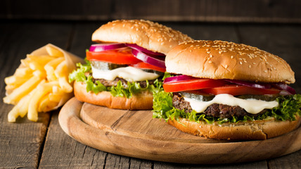 Close-up photo of home made hamburger with beer made of beef, onion, tomato, lettuce, cheese and spices. Fresh burger closeup on wooden rustic table with potato fries and chips.