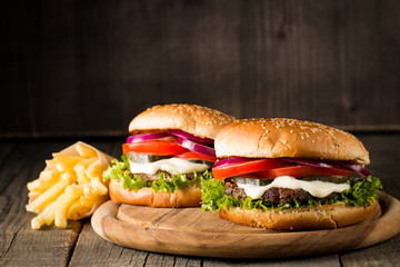 Close-up photo of home made hamburger with beer made of beef, onion, tomato, lettuce, cheese and spices. Fresh burger closeup on wooden rustic table with potato fries and chips.