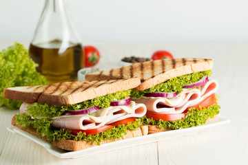 Close-up photo of a club sandwich. Sandwich with meat, prosciutto, salami, salad, vegetables, lettuce, tomato, onion and mustard on a fresh sliced rye bread on wooden background. Olives background.