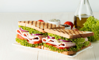 Close-up photo of a club sandwich. Sandwich with meat, prosciutto, salami, salad, vegetables, lettuce, tomato, onion and mustard on a fresh sliced rye bread on wooden background. Olives background.