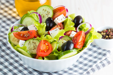 Fresh Greek salad made of cherry tomato, ruccola, arugula, feta, olives, cucumbers, onion and spices. Caesar salad in a white bowl on wooden background. Healthy organic diet food concept.