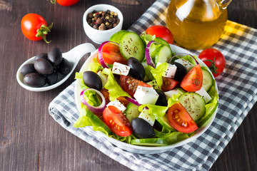 Fresh Greek salad made of cherry tomato, ruccola, arugula, feta, olives, cucumbers, onion and spices. Caesar salad in a white bowl on wooden background. Healthy organic diet food concept.