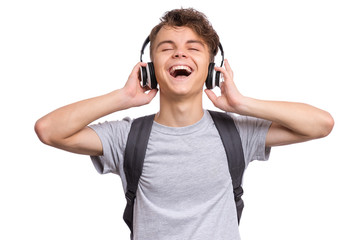 Happy teen boy with headphones and backpack, isolated on white background. Cheerful child listening to music and singing song. Emotional portrait of handsome teenager enjoying music Back to school.