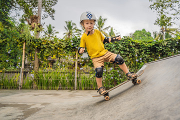 Athletic boy in helmet and knee pads learns to skateboard with in a skate park. Children education, sports © galitskaya