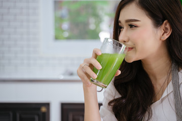 young girl drinking green cocktail with a straw.Woman drinking a homemade green detox juice. texting on her phone while sitting in her kitchen table 