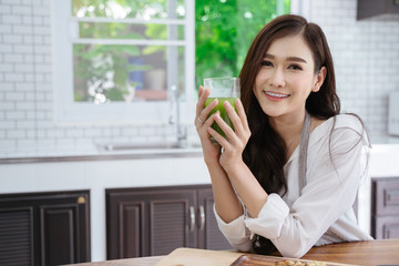 Fototapeta premium young girl drinking green cocktail with a straw.Woman drinking a homemade green detox juice. texting on her phone while sitting in her kitchen table 