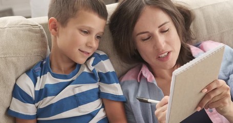 Happy mother with son planning and writing shopping list in notepad