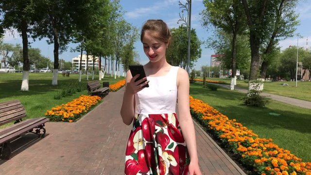 Young beautiful woman calling by phome in flowers dress walking in summer park