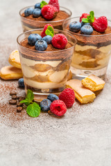 Classic tiramisu dessert with blueberries and raspberries and savoiardi cookies in a glass on concrete background