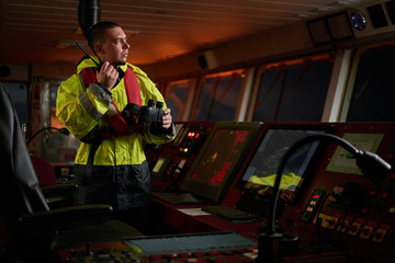 Fototapeta na wymiar Navigator. pilot, captain as pat of ship crew performing daily duties with VHF radio, binoculars on board of modern ship with high quality navigation equipment on the bridge on sunrise.