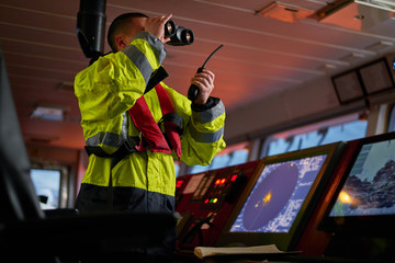 Navigator. pilot, captain as pat of ship crew performing daily duties with VHF radio, binoculars on...