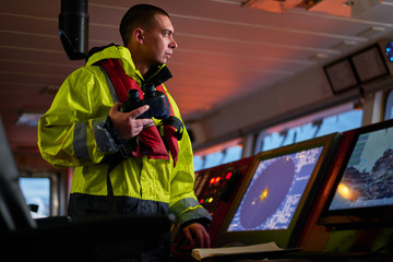 Navigator. pilot, captain as pat of ship crew performing daily duties with VHF radio, binoculars on...