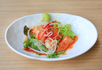 Spicy salmon salad in white plate on wooden table. Japanese food.