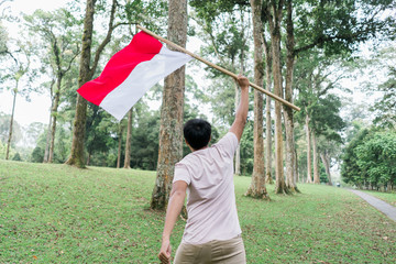 asian young man flapping Indonesian flag with spirit in the park