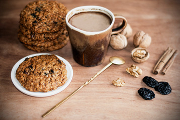 oatmeal cookies, brown mug with cocoa, walnuts, cinnamon, prunes, vintage spoon on the wooden table