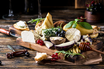 Cheese appetizer selection. Red currant, honey, basil, grapes and nuts on rustic wooden board over wooden concrete backdrop, top view. Belper Knolle, goat cheese, Scamorza. Cheese board, cheese plate