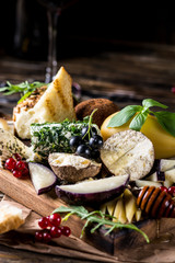 Cheese appetizer selection. Red currant, honey, basil, grapes and nuts on rustic wooden board over wooden concrete backdrop, top view. Belper Knolle, goat cheese, Scamorza. Cheese board, cheese plate