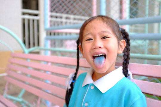 Cheeky Funny Face Little Asian Child Girl Smile And Poking Out Blue Colored Tongue. Food Coloring In Children Sweets.