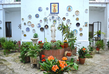 Obraz na płótnie Canvas Patio of an Andalusian house with water well decorated with flower pots and religious images of Jesus Christ and the Virgin