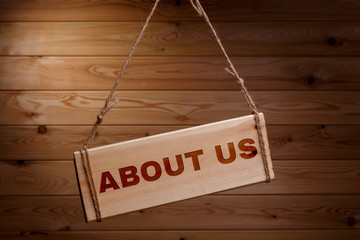 Wooden signboard with the words ABOUT US on a rough rope on a beautiful wooden background