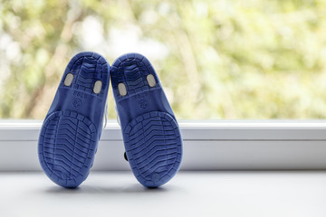 Childrens shoes on a white windowsill, against a light landscape outside the window