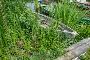 Street view, abandoned broken wooden fishing boat hidden in grass, Ioannina island on lake Pamvotida near the beautiful small island near Greek town of Ioannina. Early morning dark spring day scene