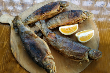 Grilled trout on a wooden round board with lemon slices top view. Whole carcasses of fried fish with lemon.