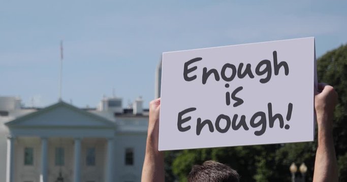 A man holds an Enough is Enough protest sign in front of the White House on a sunny summer day.	 	