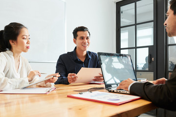 Two business colleagues sitting at the table and listening to their male leader while he using laptop computer at office