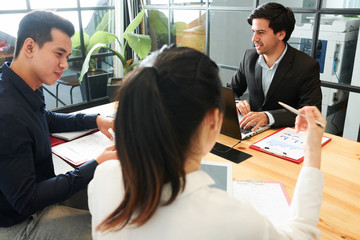 Group of business people sitting at the table working with laptop and documents and discussing...
