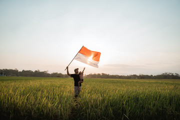 asian young father with daughter flapping Indonesian flag with spirit in the rice field