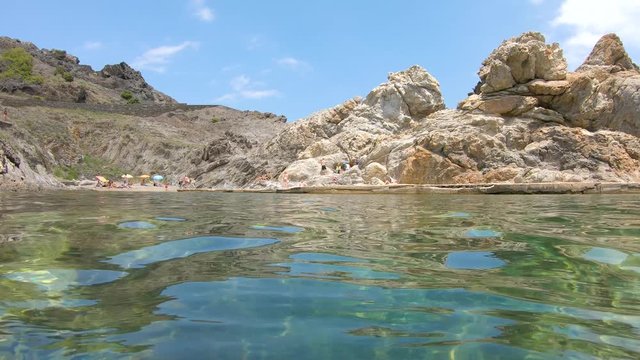 Spain Costa Brava, Cap de Creus, Mediterranean cove on rocky coast with boats moored seen from sea surface and moving camera down underwater, Cala Culip, Catalonia, panning shot