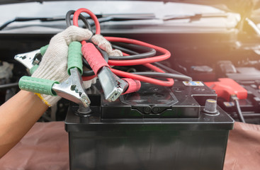 Car mechanic hands in gloves is ready charging a discharged battery with booster jumper cables in the garage.