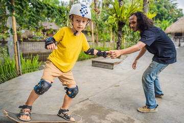 Athletic boy learns to skateboard with a trainer in a skate park. Children education, sports