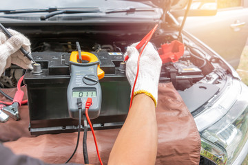Mechanic car service using Multimeter to check the voltage level in a car battery