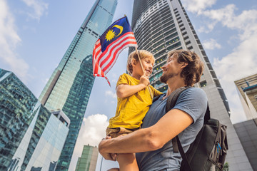 Dad and son tourists in Malaysia with the flag of Malaysia near the skyscrapers. Traveling with kids concept