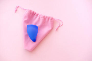 Blue menstrual cup and bag on pink background. Bag shaped as uterus. Feminine hygiene alternative product. Menstruation, critical days, woman period. Women health concept